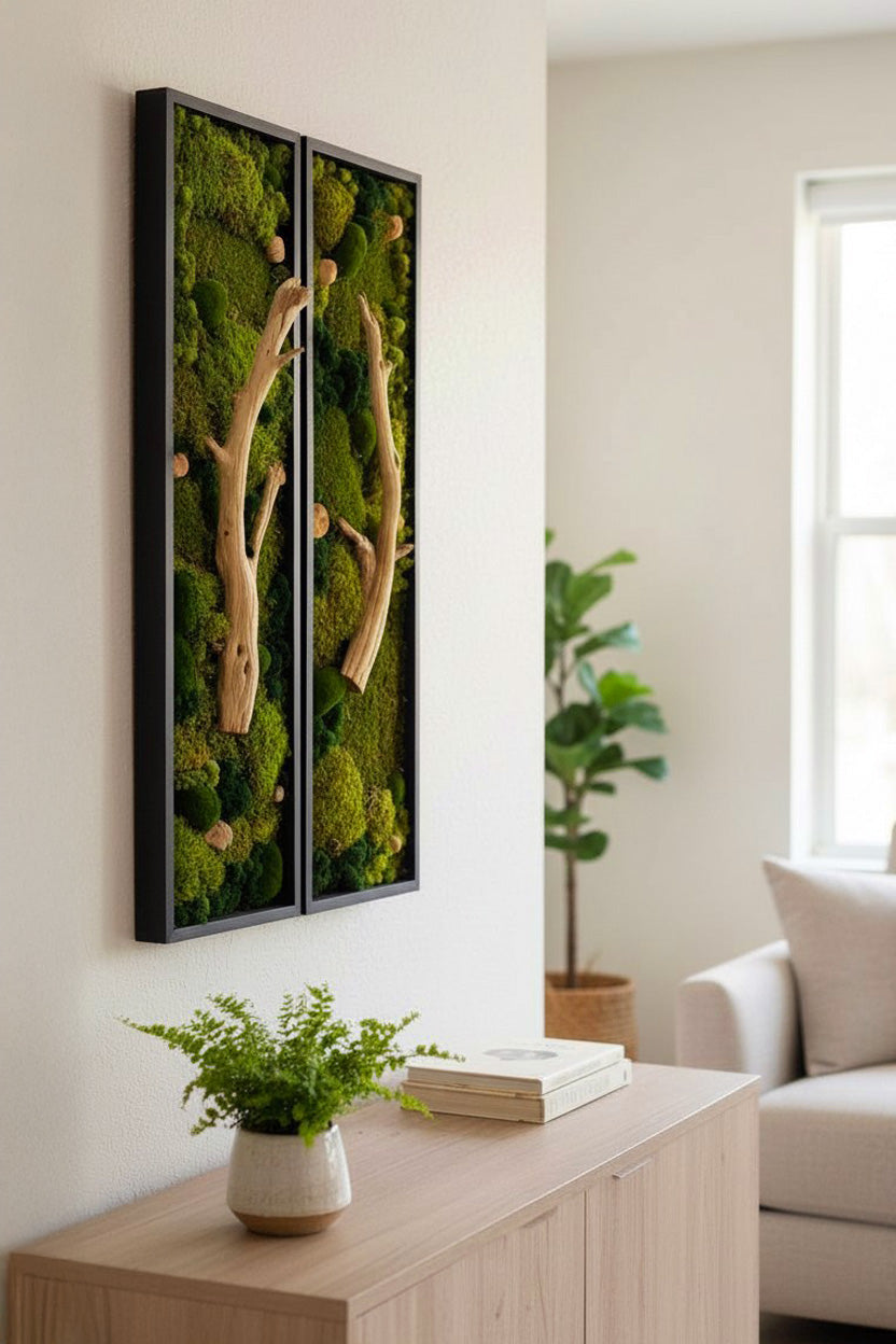 Two framed moss wall art pieces on a white wall above a wooden console table with a plant and books.